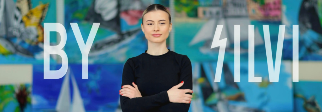 Portrait of Silvi The Artist standing confidently in front of her contemporary abstract paintings with “By Silvi” branding.
