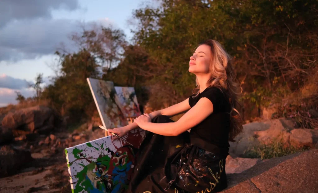 Silvi The Artist resting outdoors at sunset with her abstract painting, reflecting on her creative process in nature.
