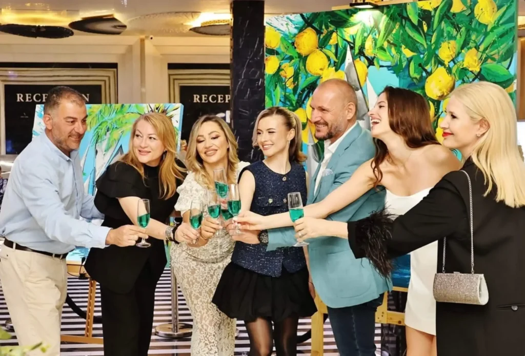 Guests celebrating at an art exhibition by Silvi The Artist, raising glasses in front of her vibrant contemporary paintings.
