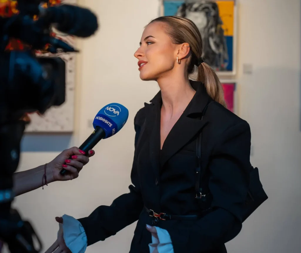Silvi The Artist giving a media interview at her exhibition, speaking about her contemporary abstract art.

